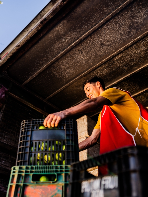 Young man unloading fruit from large truck.