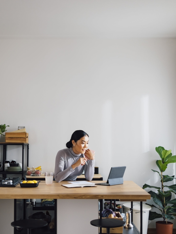 Woman sitting in small home kitchen taking notes on misclassification risk from tablet.