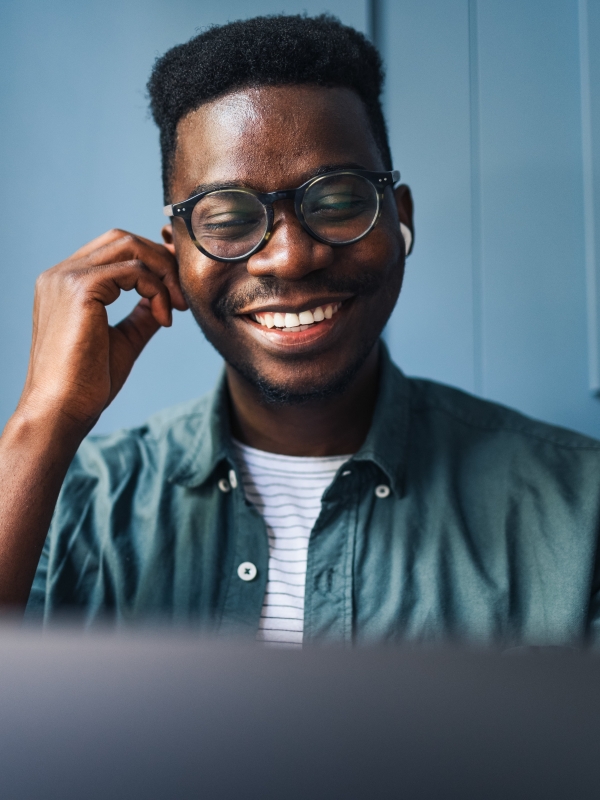 Male employer smiling and adjusting airpods while looking at computer with blue background.