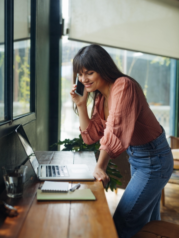 Female employer on cell phone discussing contractor conversion while looking at laptop.