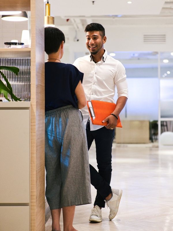 Two H1B visa employees at an AI company smiling and chatting while holding a laptop