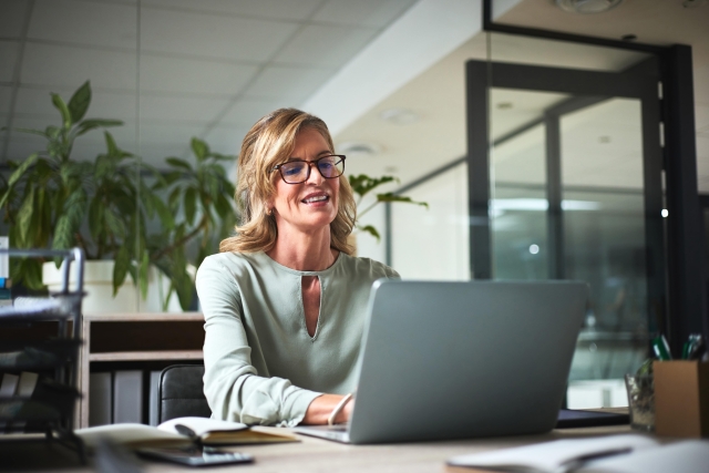 Woman researching global Employer of Record services on laptop in business casual office setting.