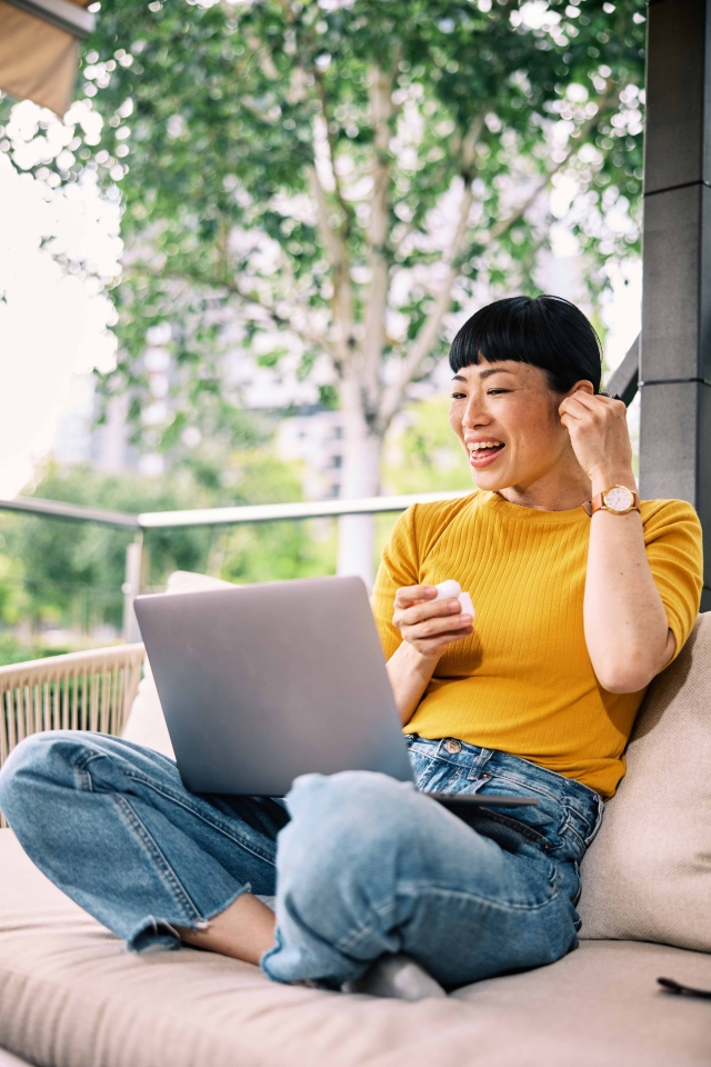Female contractor sitting outside, putting airpod in her ear with laptop in lap.