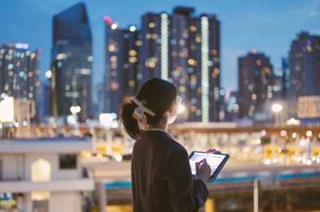 Female employer holding tablet while looking over city skyline at night.