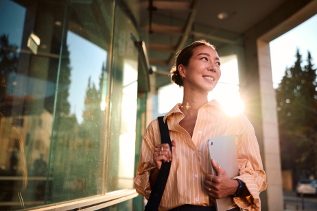 Portrait style image of professional woman in outdoor setting holding bag and tablet.