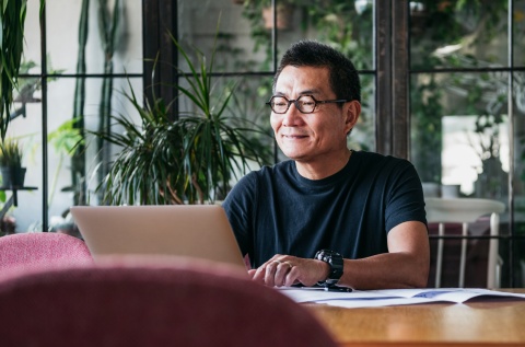 Man sitting at desk smiling while working on a laptop