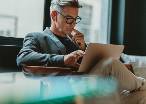 A male HR professional works on his laptop while seated in a chair in an office space