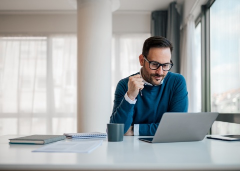 Male professional working asynchronously and remotely from a laptop while sitting in a day-lit home office
