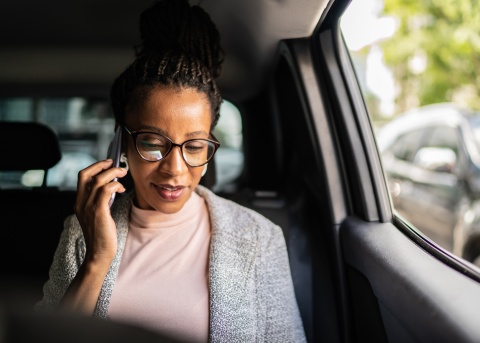 Female professional talking on her mobile phone while sitting in a car and traveling abroad for a business trip