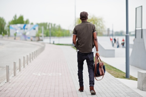 Back view of man holding backpack & walking along brick path