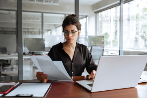 Businesswoman holding documents while working on her laptop on payroll taxes in Gabon