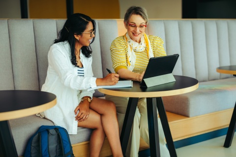 Two women together using a digital tablet discussing payroll taxes in Panama