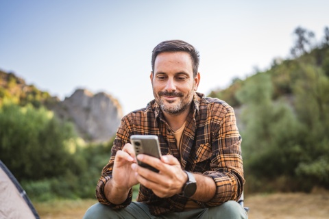 A man sitting in front of a tent using his mobile phone on a camping trip