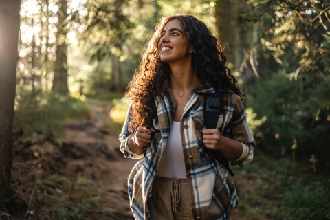 Cheerful woman with a backpack hiking on a forest path