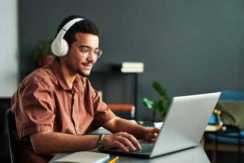 Young smiling man with headphones on typing on laptop