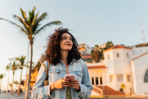 Young woman looking away, holding a mobile phone outdoors