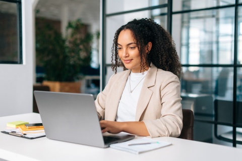 Curly haired woman using laptop while sitting at her workplace in South America
