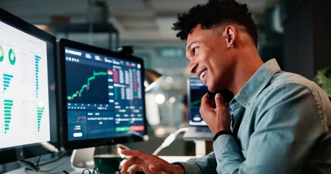 Male financial analysts working on two computer monitors