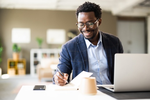 Male legal assistant writing in a notebook while working in office