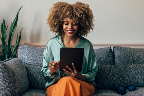 A woman sitting on a couch at home, smiling while browsing for Rippling alternatives for payroll and EOR solutions