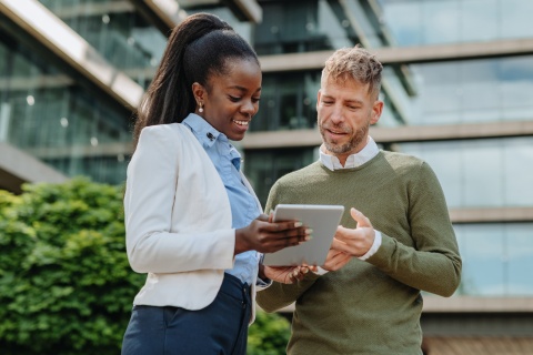 Two colleagues reviewing a tablet outside an office, using compensation management software.