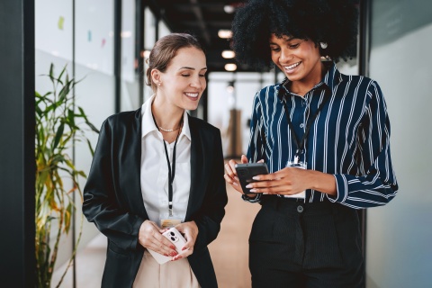 Two smiling colleagues looking at a phone in an office, discussing OTE salary.