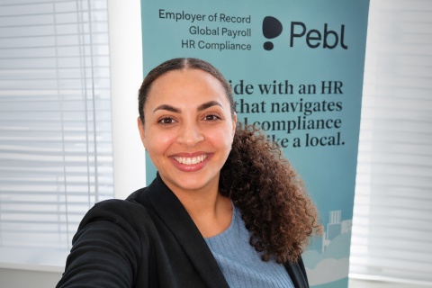 Solange Obawole, a Black woman with warm brown skin and naturally curly hair pulled into a ponytail, smiling at the camera in a blue top and business jacket, with a Pebl banner in the background. 
